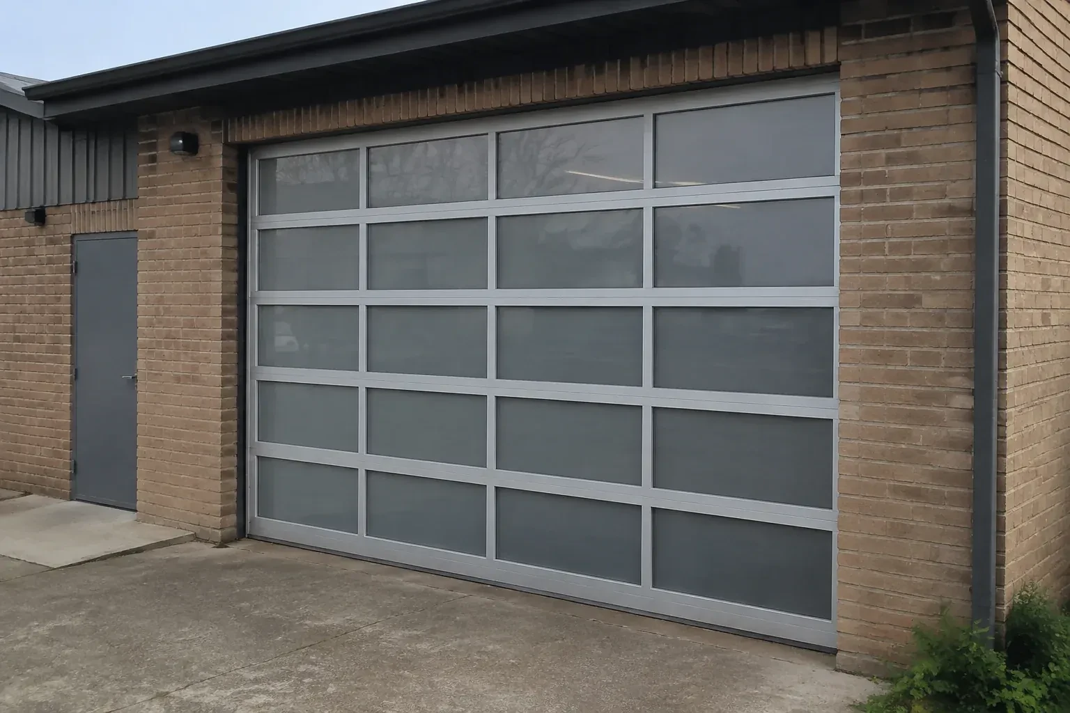 Closed glazed sectional door in a grey metal frame at a brick workshop. — Full-View Glass Garage Door Installation, Essa